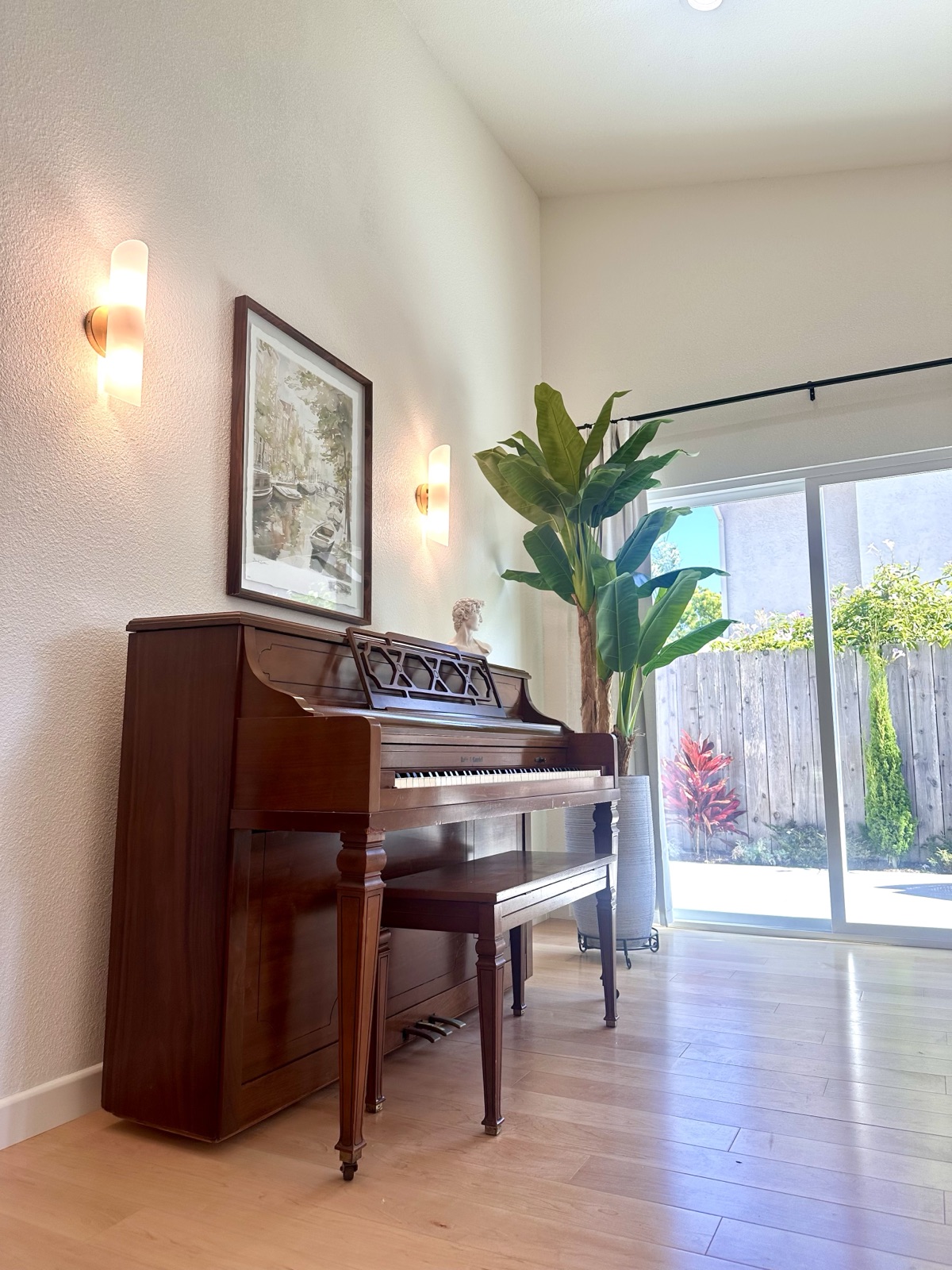 Piano corner with lit wall sconces and a garden-view sliding door